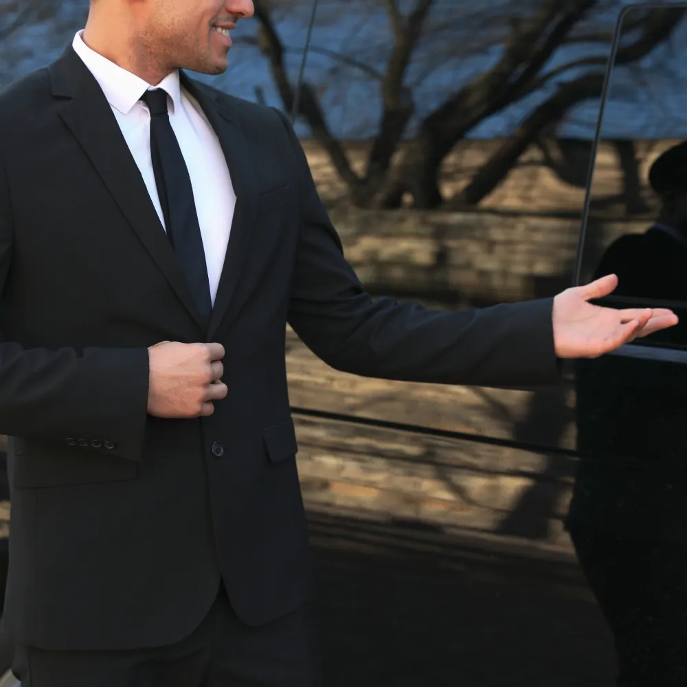 Chauffeur privé VTC en costume, accueillant devant un van noir pour transfert aéroport à Canne-Mandelieu, Côte d’Azur.